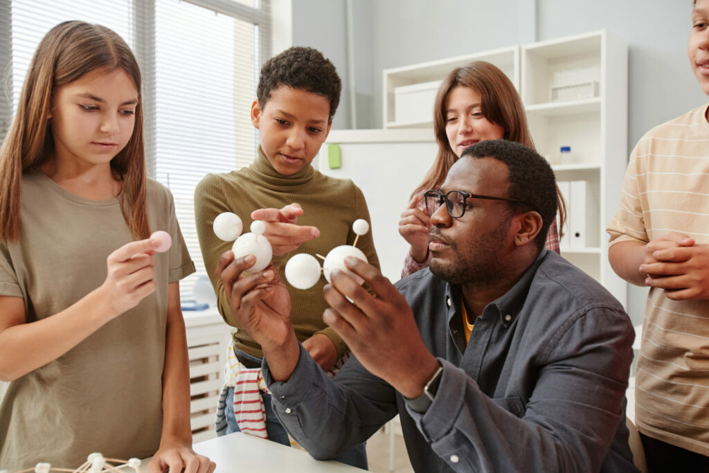 Side view portrait of African American teacher explaining molecule structure to diverse group of children in chemistry class