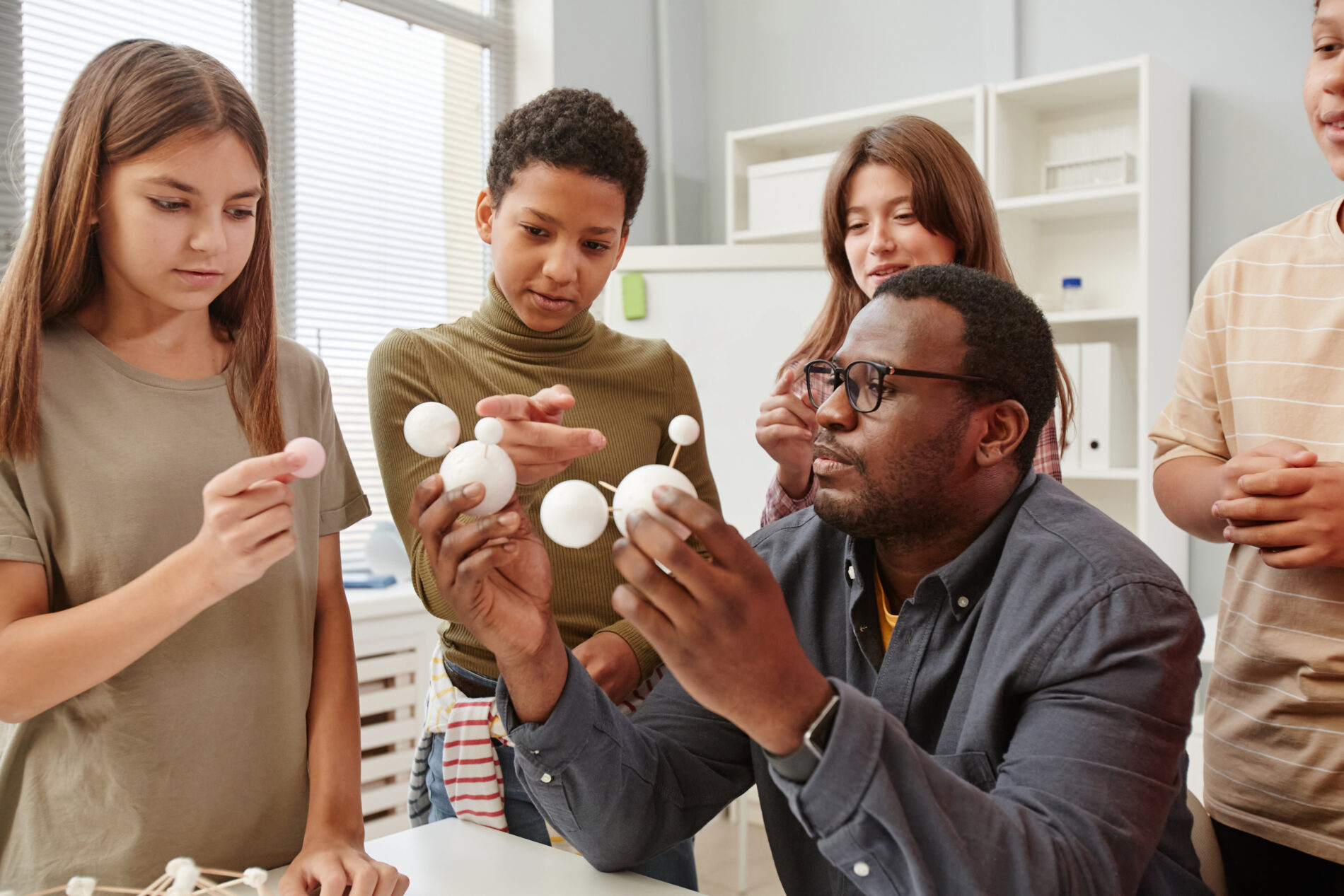 Side view portrait of African American teacher explaining molecule structure to diverse group of children in chemistry class